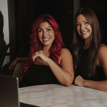 Zwei Frauen des Secret Creators Club lächeln an einem Tisch mit Laptop